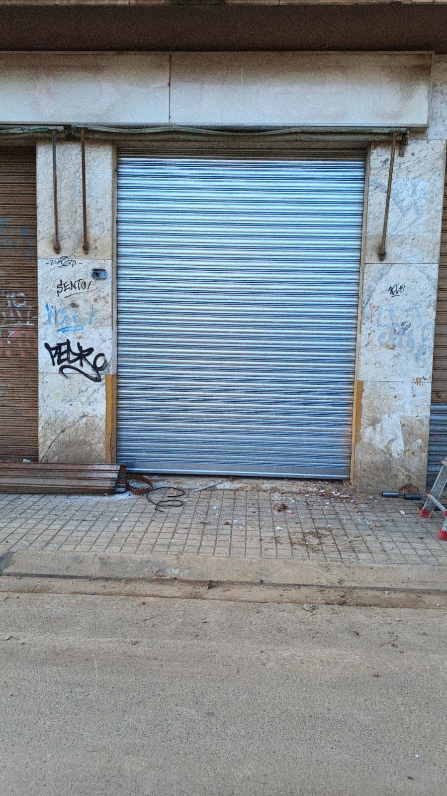 Persiana de escaparate de metal pintada con un patrón de ondas horizontales de color azul/gris, rodeada de piedra desgastada.