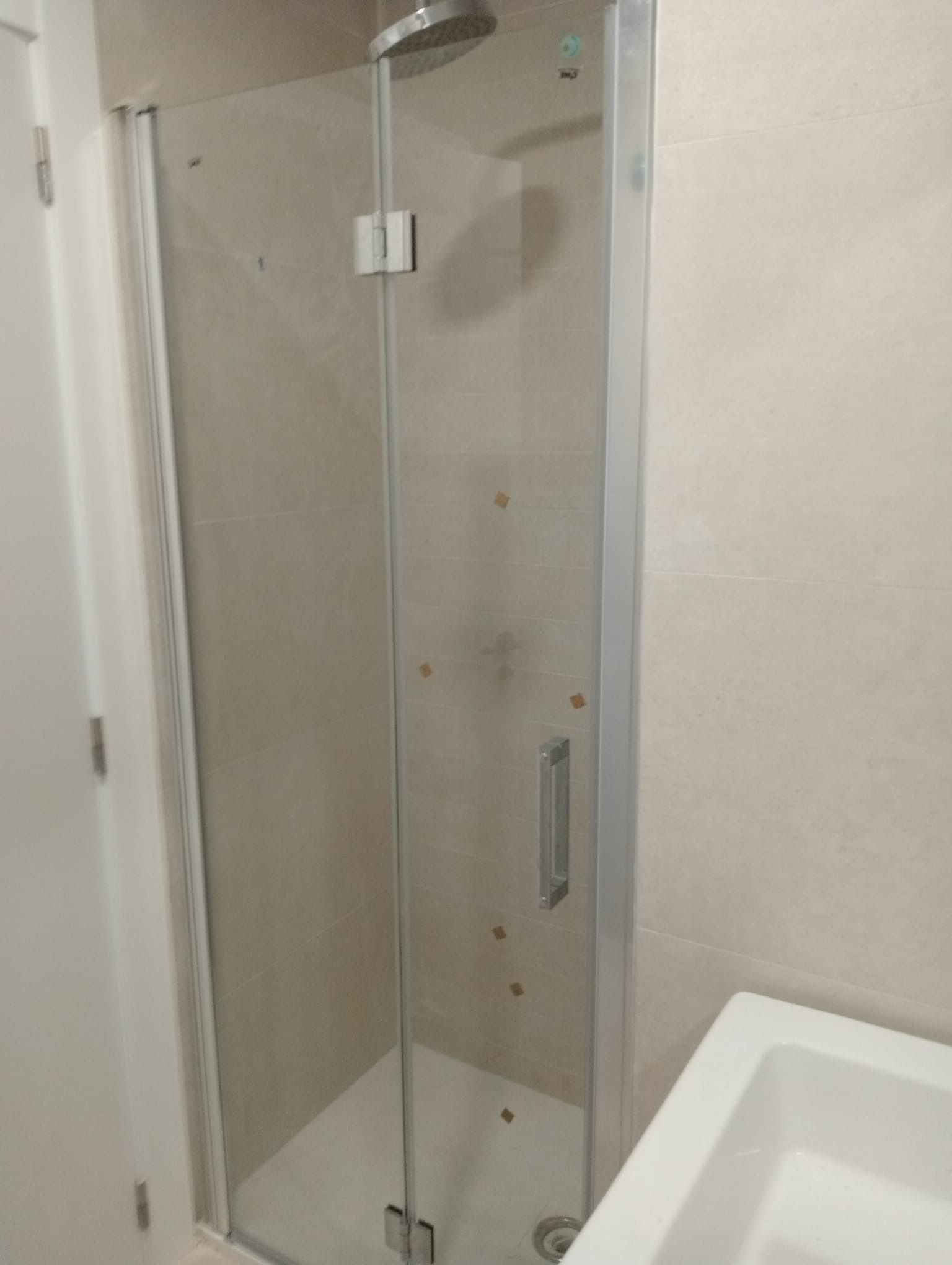 Cabina de ducha con puerta de cristal, manija plateada y cabezal de ducha en un baño.