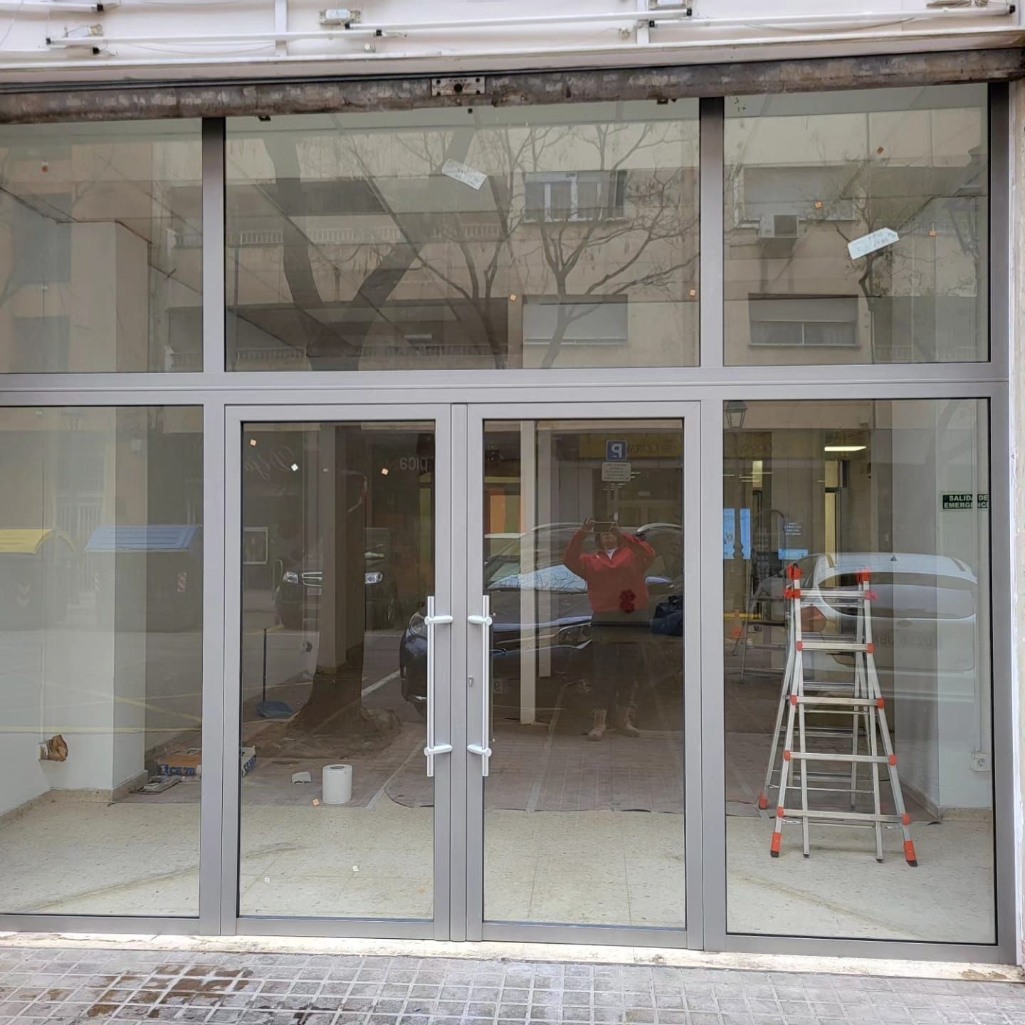Fachada de local con puertas y ventanas de cristal, en construcción, con escalera en su interior.