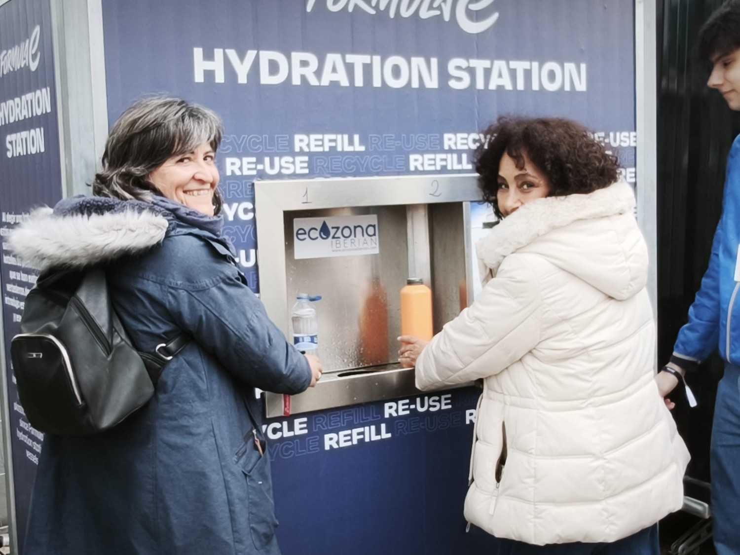 Dos personas usando una estación pública de agua para rellenar botellas y vasos reutilizables