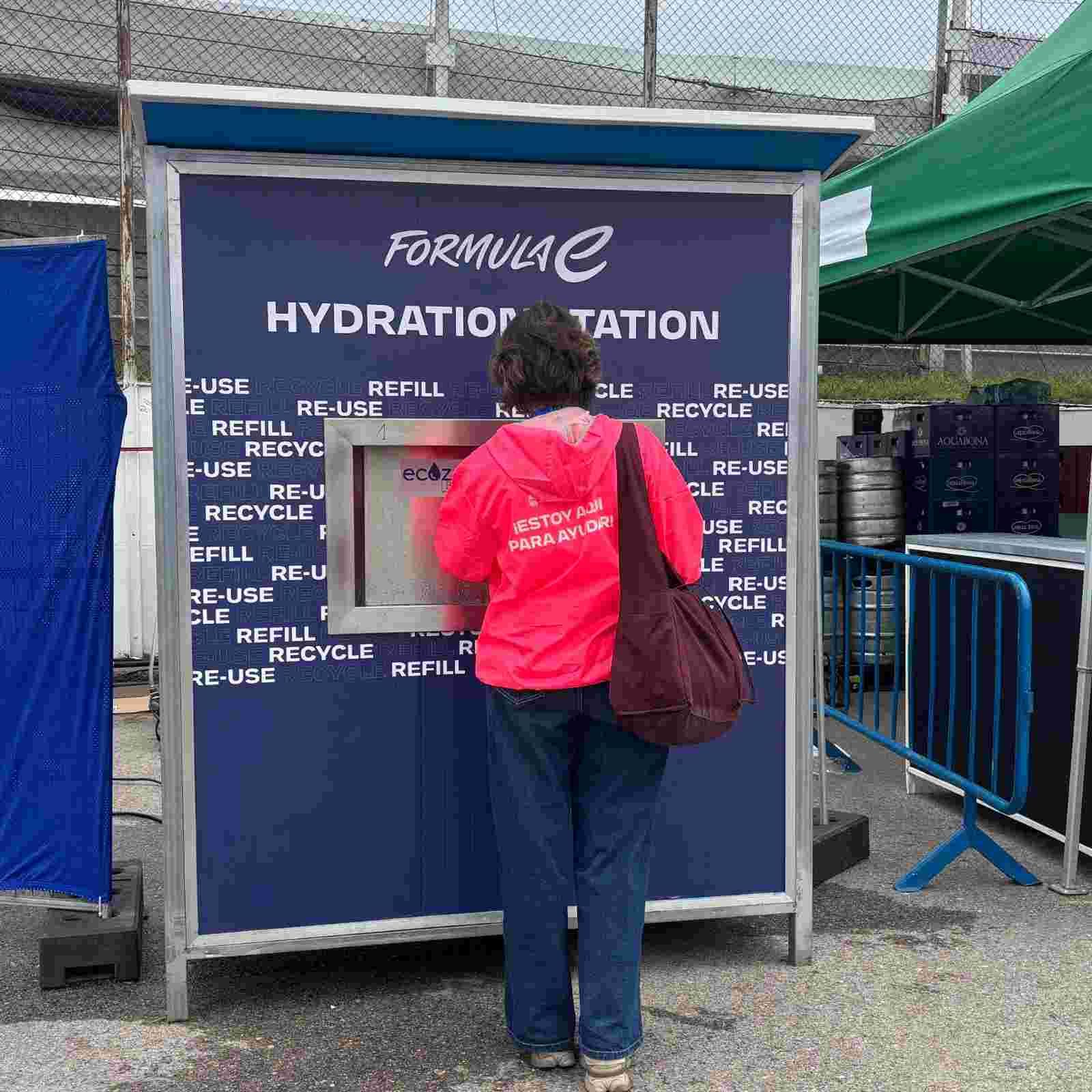 Una persona con camiseta roja usando un punto de hidratación en un evento al aire libre