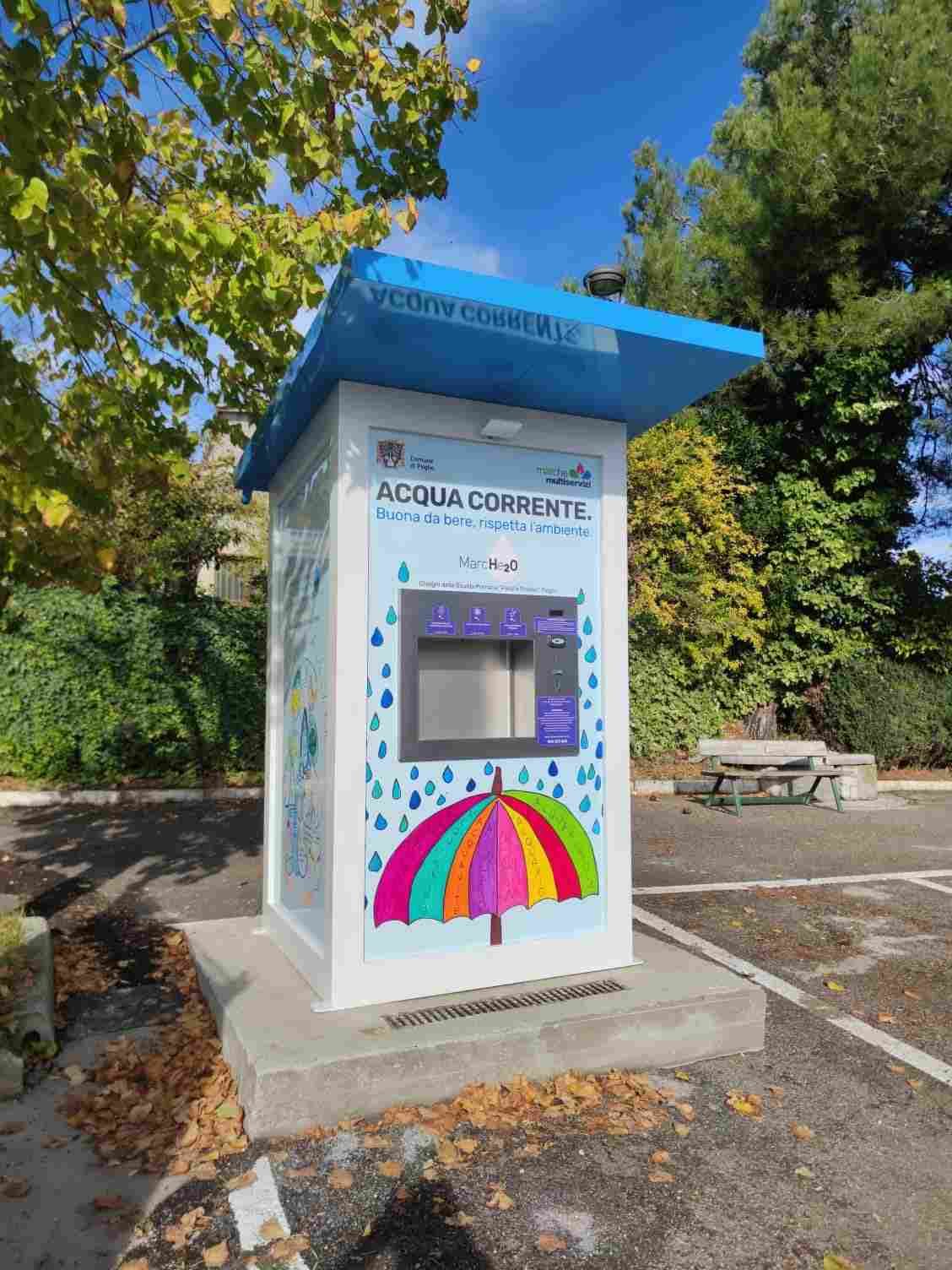 Quiosco azul y blanco en una acera con murales, cerca de coches aparcados y árboles.