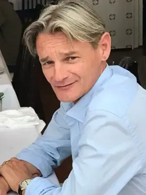 Una persona con una camisa azul claro está sentada a una mesa, mirando a la cámara con una leve sonrisa.