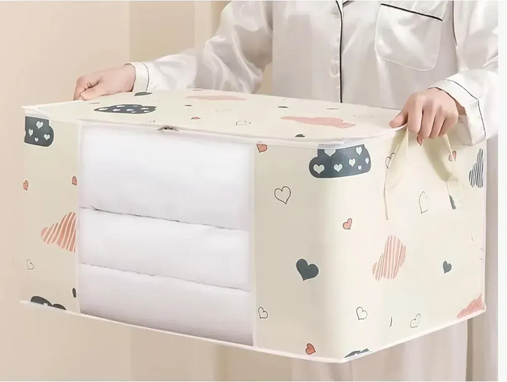 Persona sosteniendo una bolsa de almacenamiento color crema llena de ropa de cama blanca. La bolsa tiene estampados de corazones y nubes de colores.