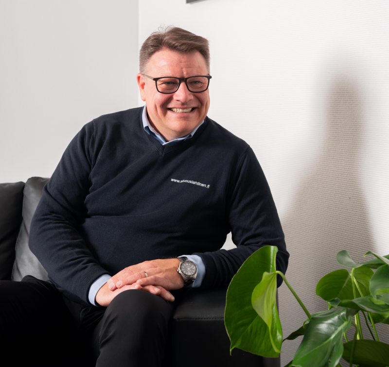 Moderni valkoinen talo mustilla yksityiskohdilla ja puisella terassilla, sininen taivas yläpuolella.