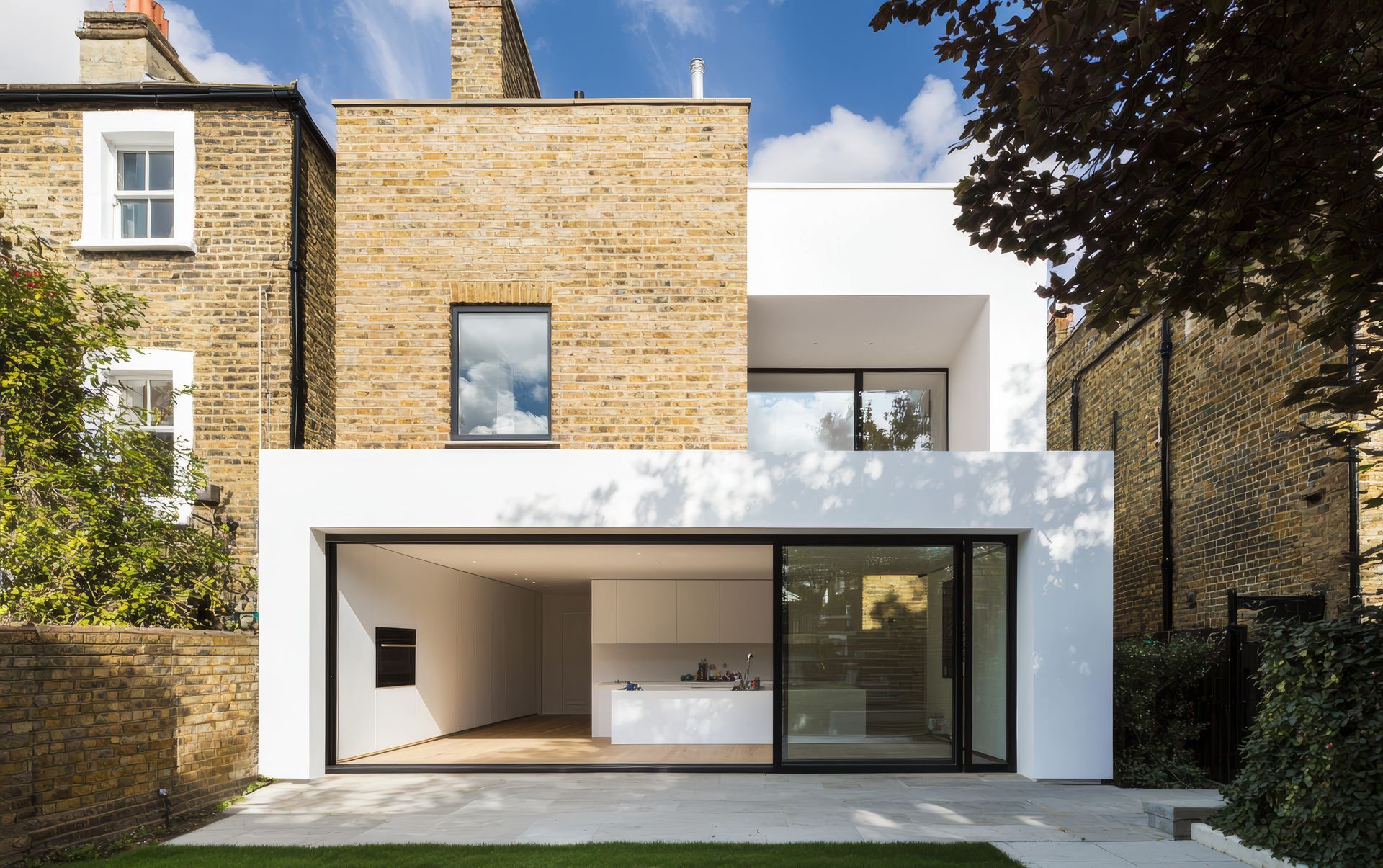 Maison moderne blanche et en briques, avec de grandes baies vitrées.