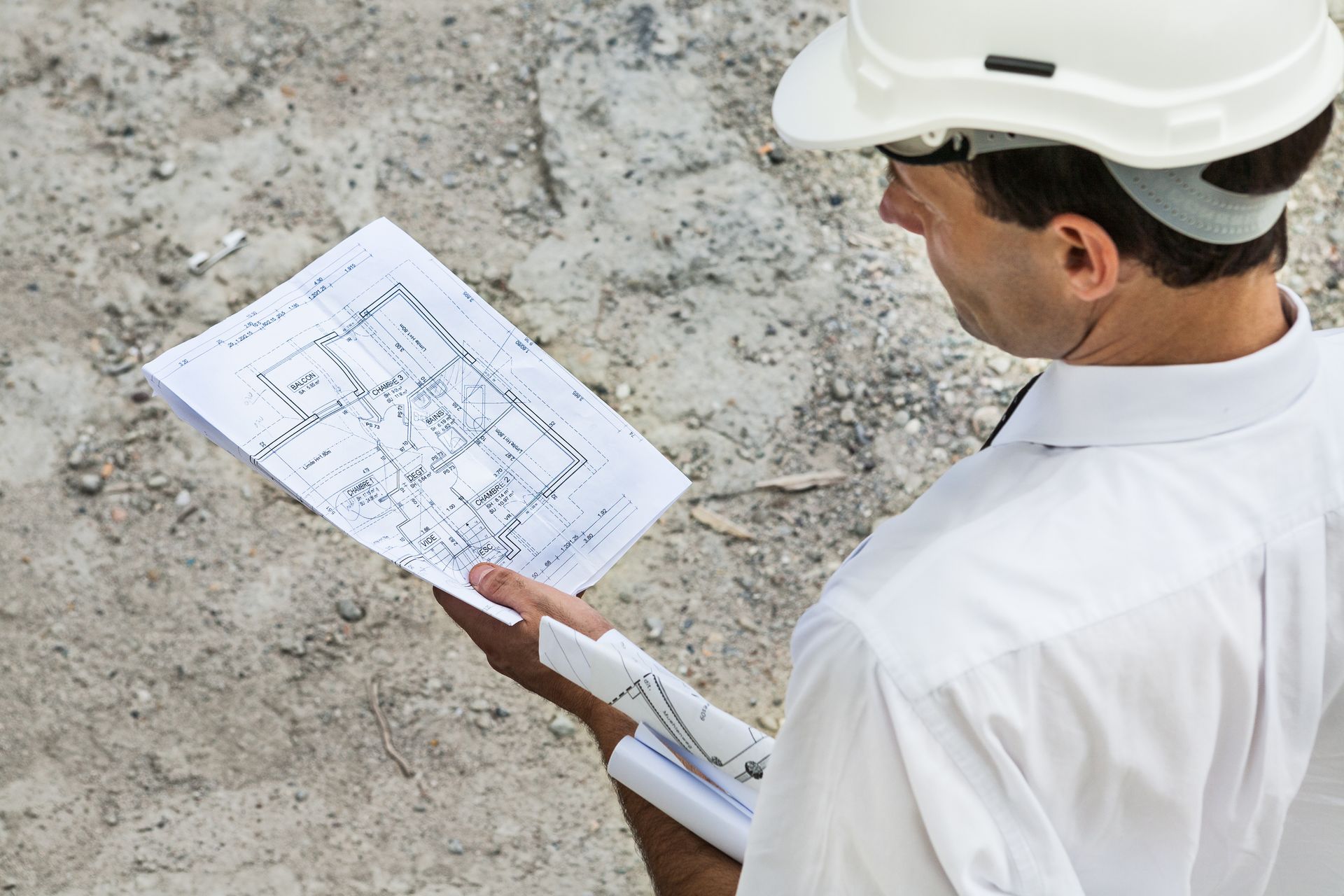 Ouvrier portant un casque blanc et consultant un plan sur un chantier de construction.