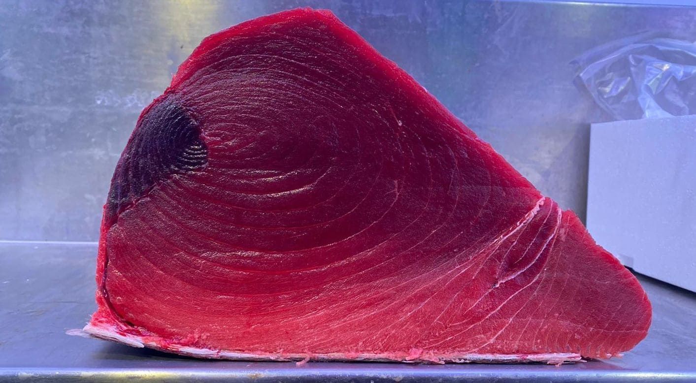 Un gran trozo de carne roja reposa sobre una bandeja de metal.