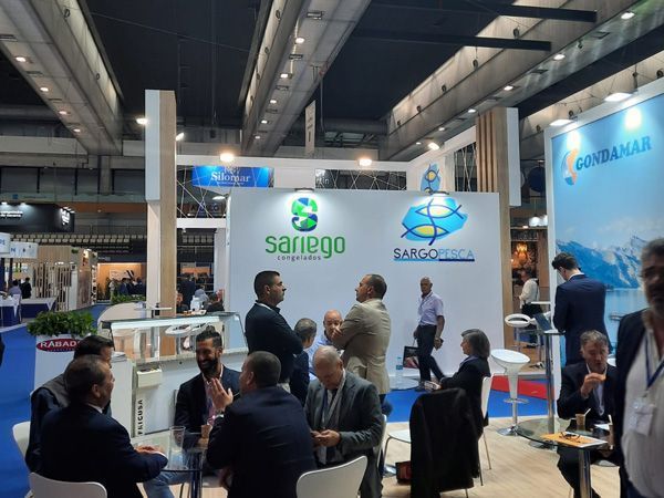 Un grupo de personas están sentadas en mesas frente a un cartel que dice sarigo