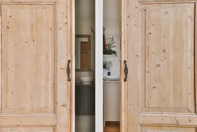 Dos puertas de madera se abren a un baño con lavabo y espejo.