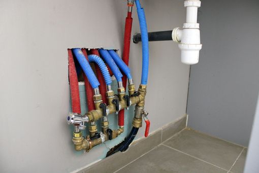 Collecteur de plomberie avec des conduites d'eau rouges et bleues et des vannes à côté d'un tuyau d'évacuation blanc dans un coin.