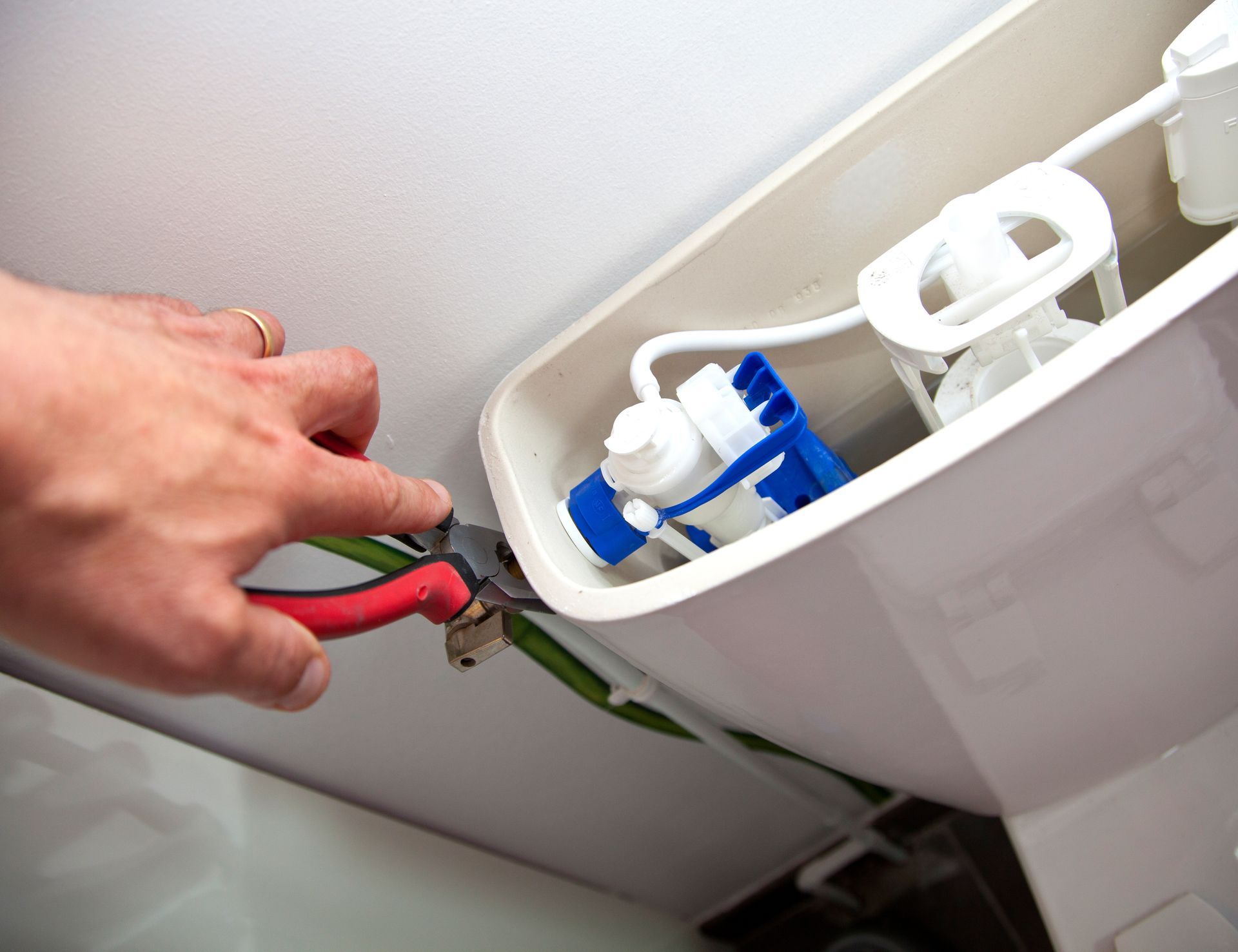 Main utilisant une pince pour serrer le robinet du réservoir de toilettes à l'intérieur de la zone du couvercle de réservoir ouvert