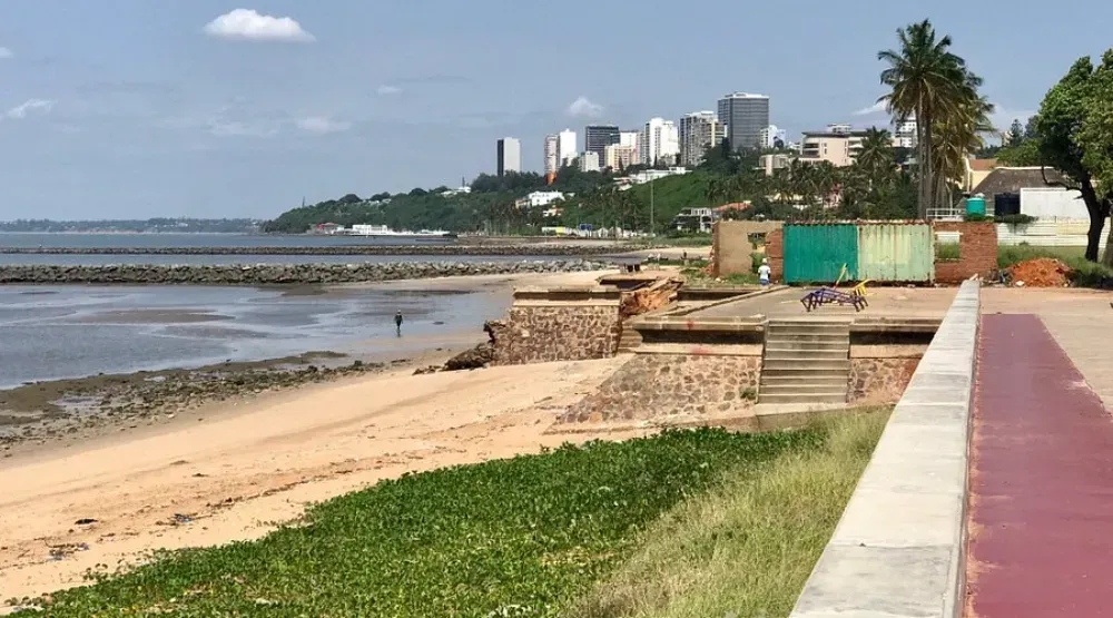 A concrete walkway leading to a beach with a city in the background.