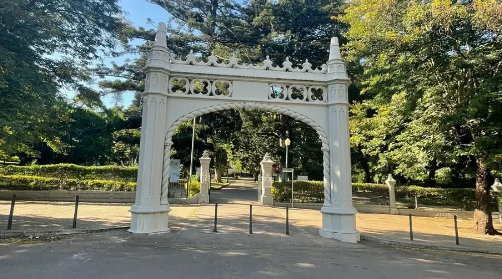 A white archway in a park with trees in the background.