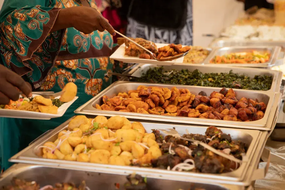 A woman is taking a plate of food from a buffet line.