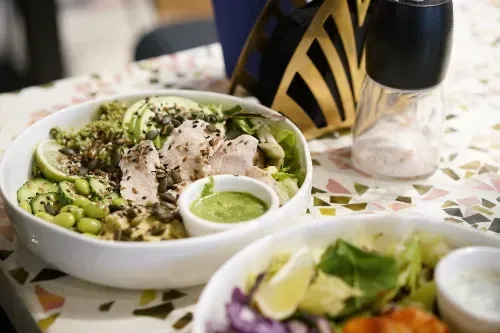 Two bowls of food are sitting on a table next to a salt and pepper shaker.