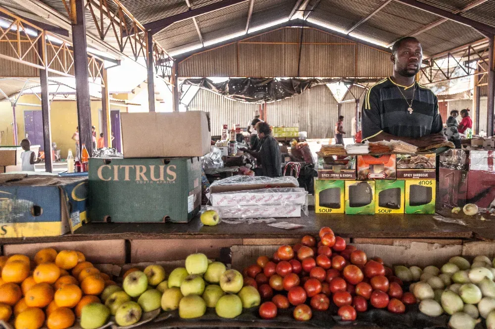 Um homem está parado atrás de uma barraca de frutas com uma caixa que diz