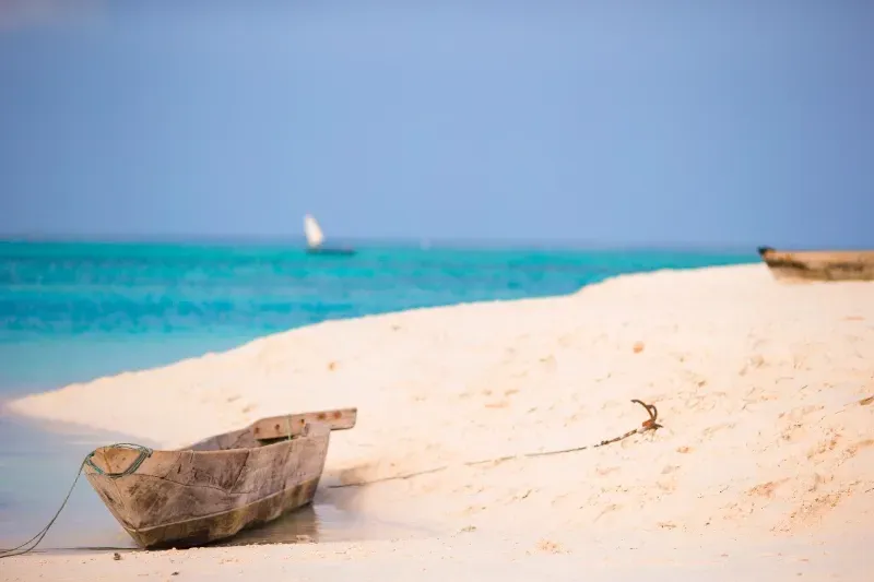 A boat is sitting on a sandy beach next to the ocean.