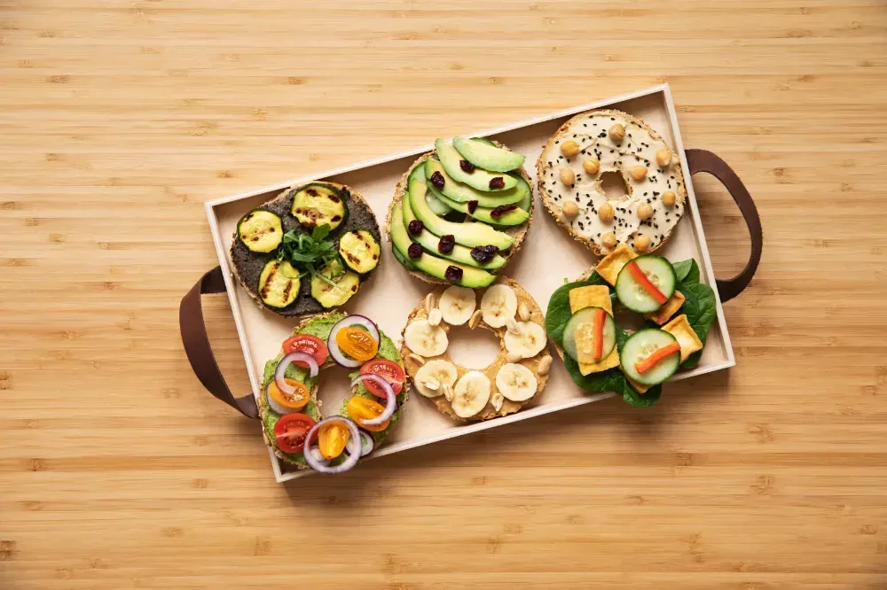 A wooden tray filled with sandwiches and vegetables on a wooden table.