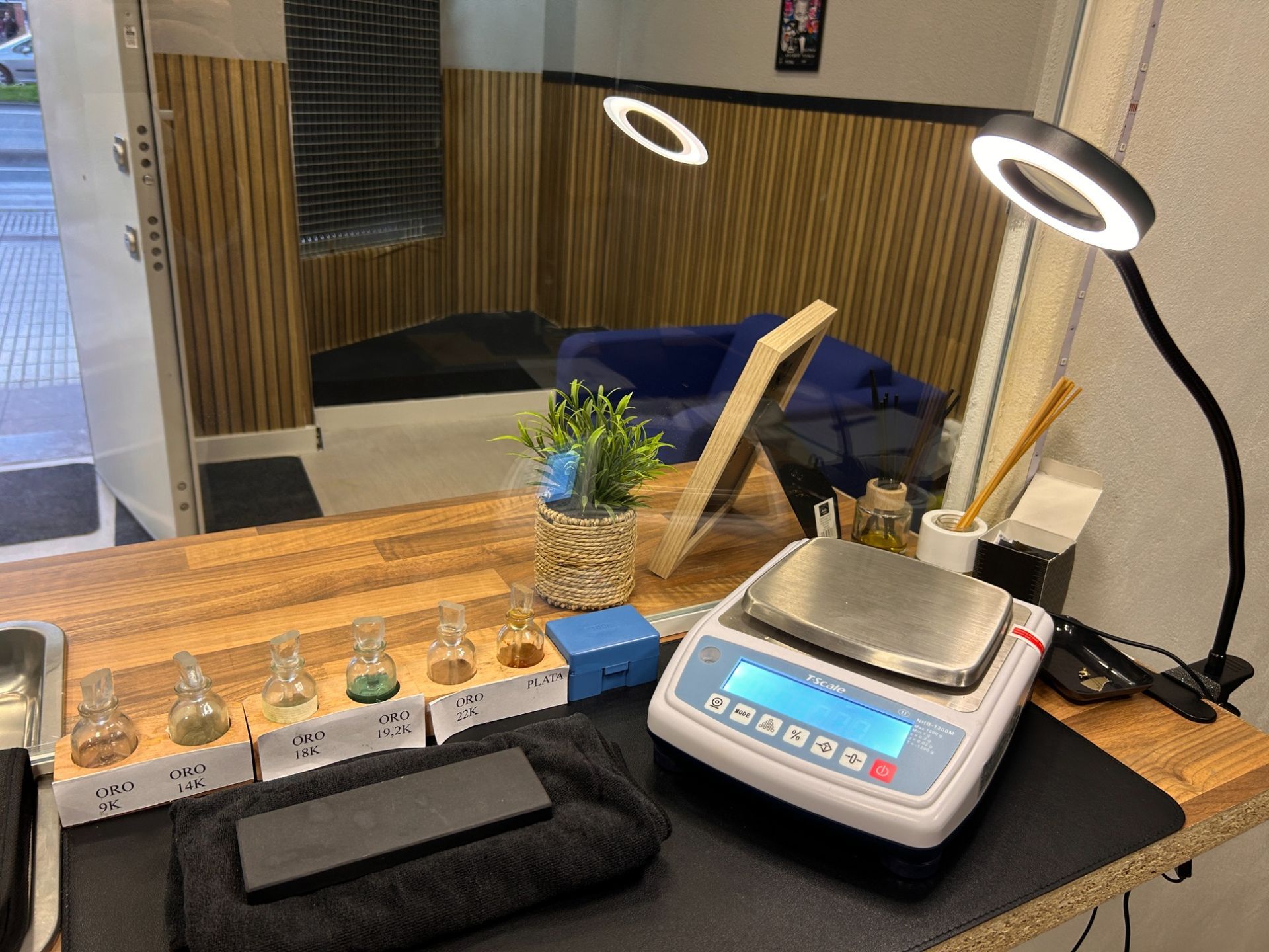 Escritorio con una báscula digital, una lámpara y pequeños frascos junto a una bandeja de madera
