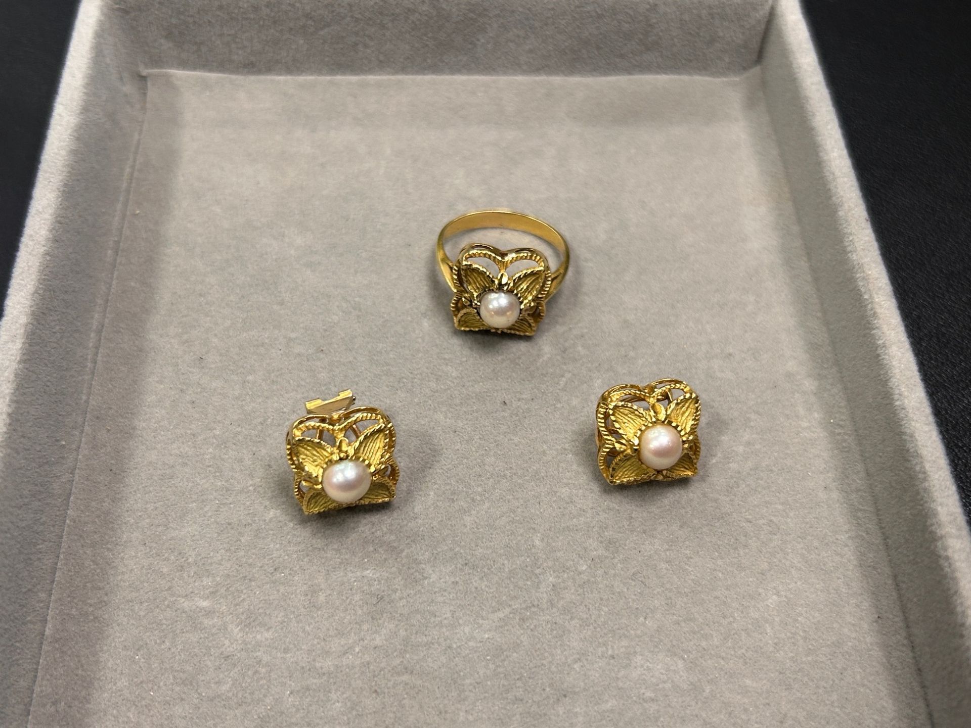 Tres anillos de oro con piedras transparentes expuestos en un joyero gris.