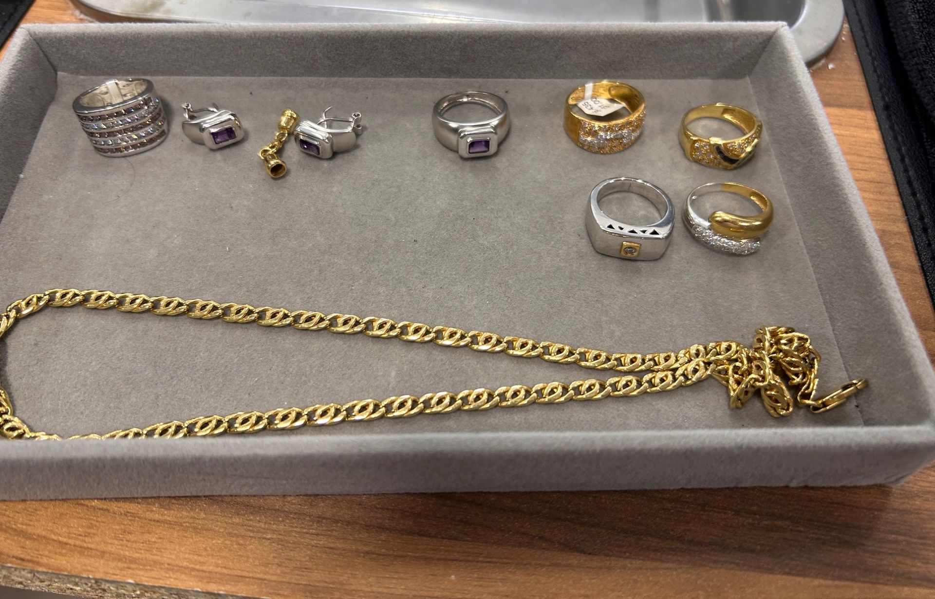 Bandeja de joyería con anillos de oro y plata y una cadena de oro sobre fieltro gris.