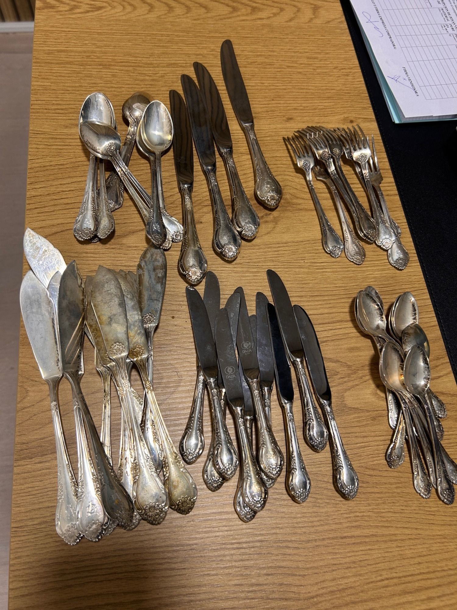 Cubiertos variados plateados y negros dispuestos en grupos sobre una mesa de madera