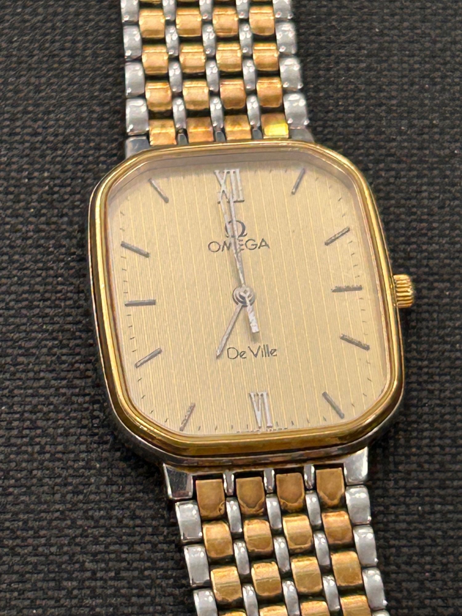 Reloj de pulsera Omega De Ville dorado con brazalete bicolor sobre un fondo claro