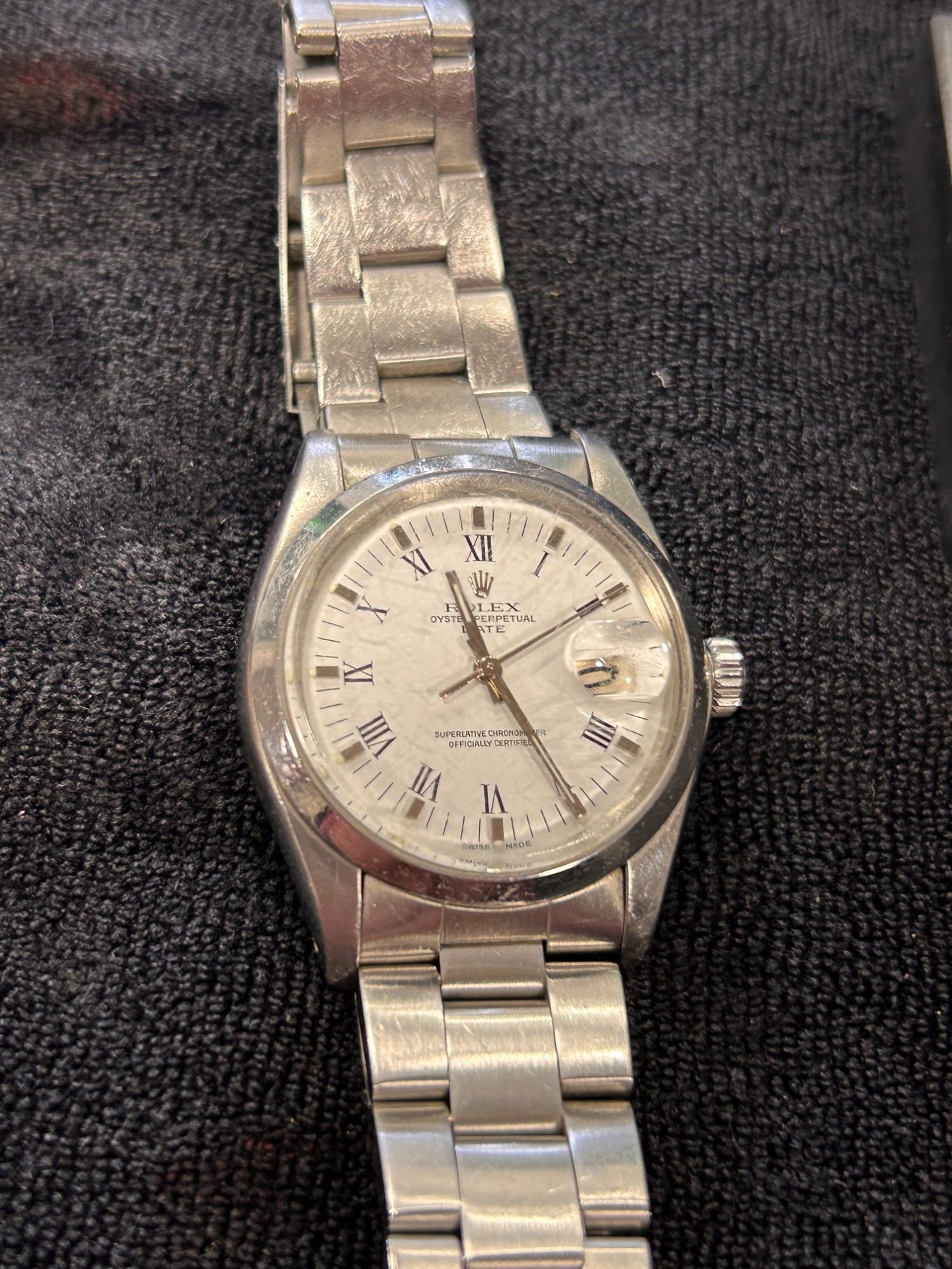 Reloj de pulsera plateado con esfera blanca y correa metálica sobre un fondo de tela oscura