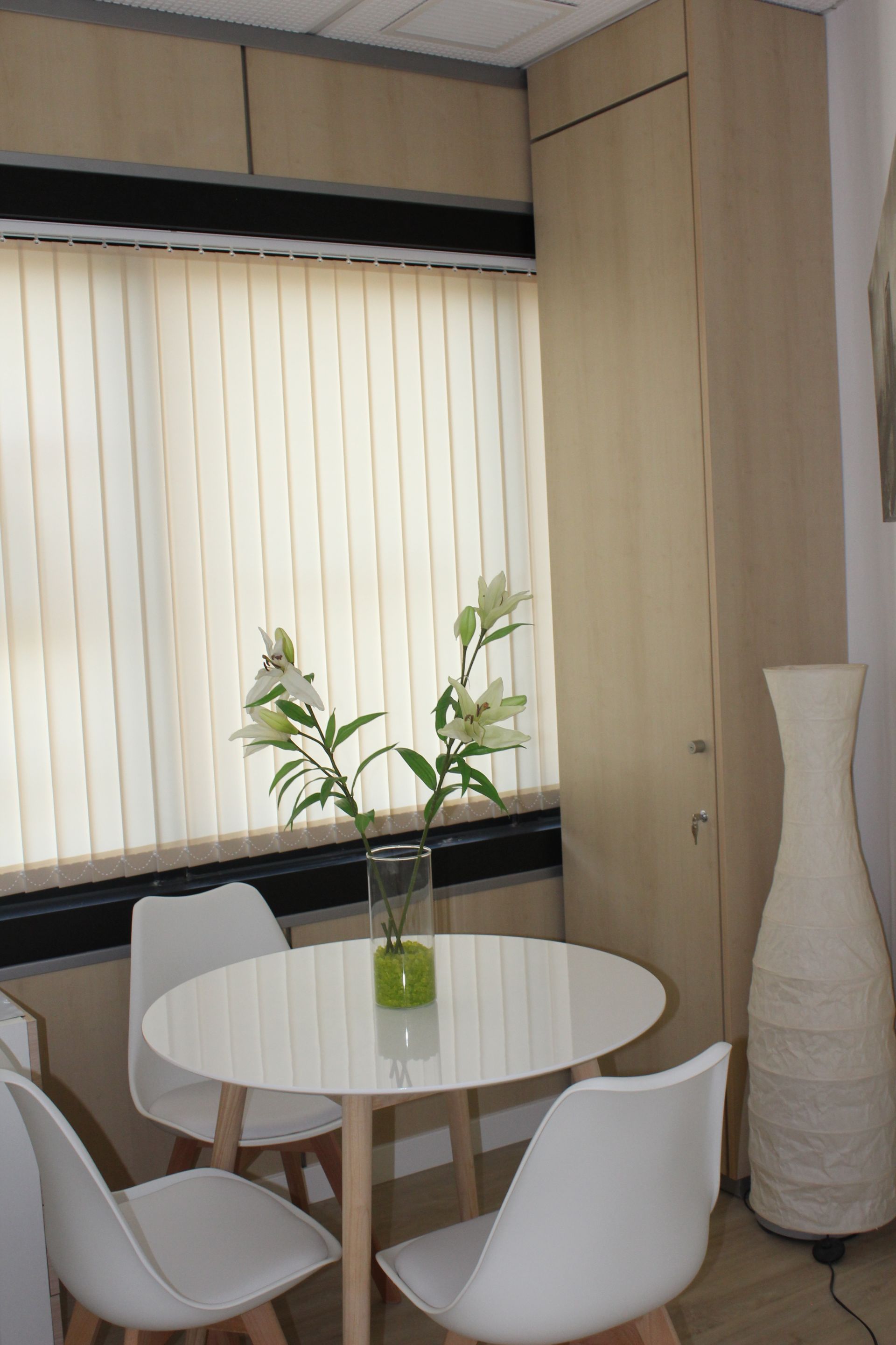 Una mesa con un jarrón de flores delante de una ventana.