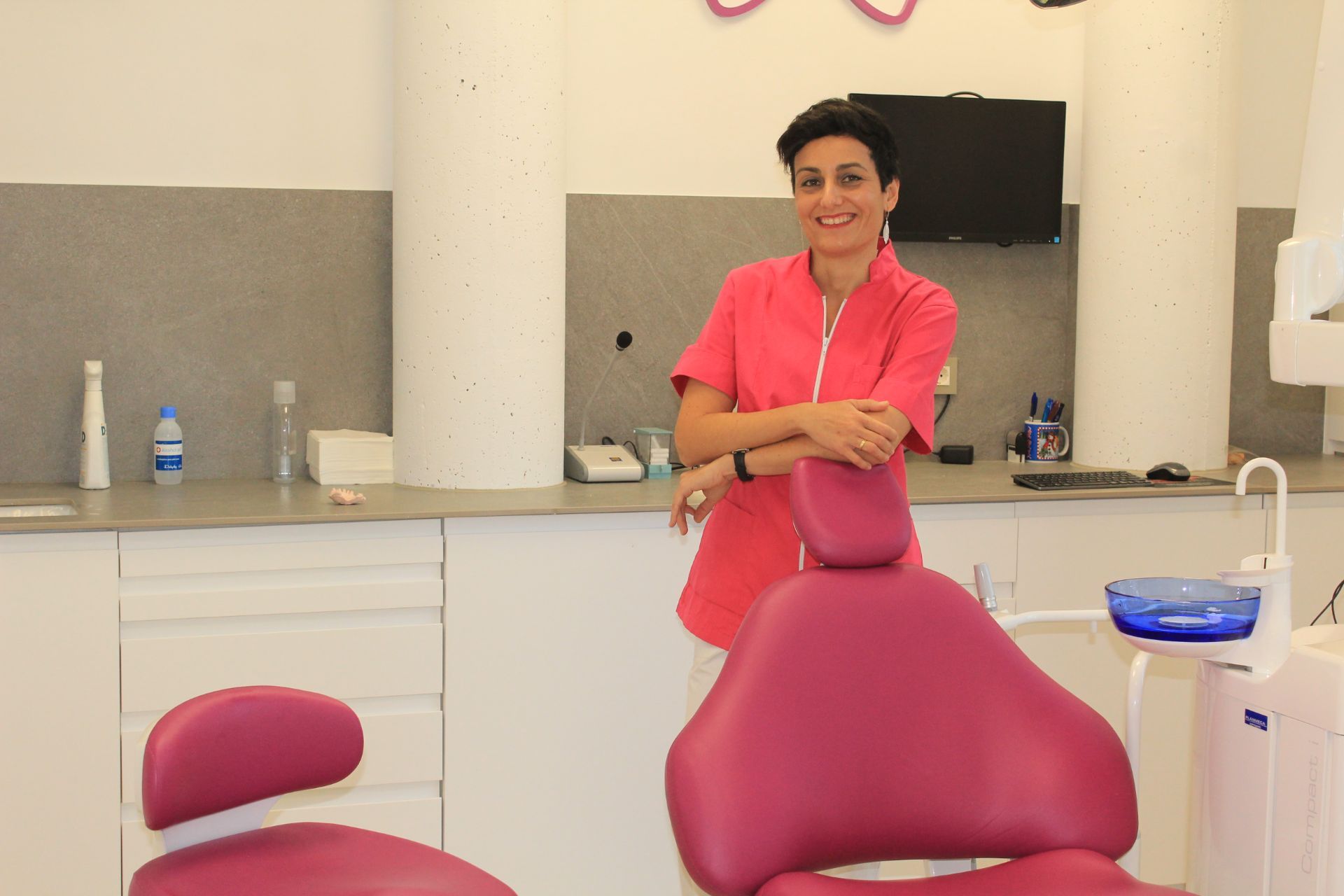Una mujer está de pie junto a una silla dental en un consultorio dental.