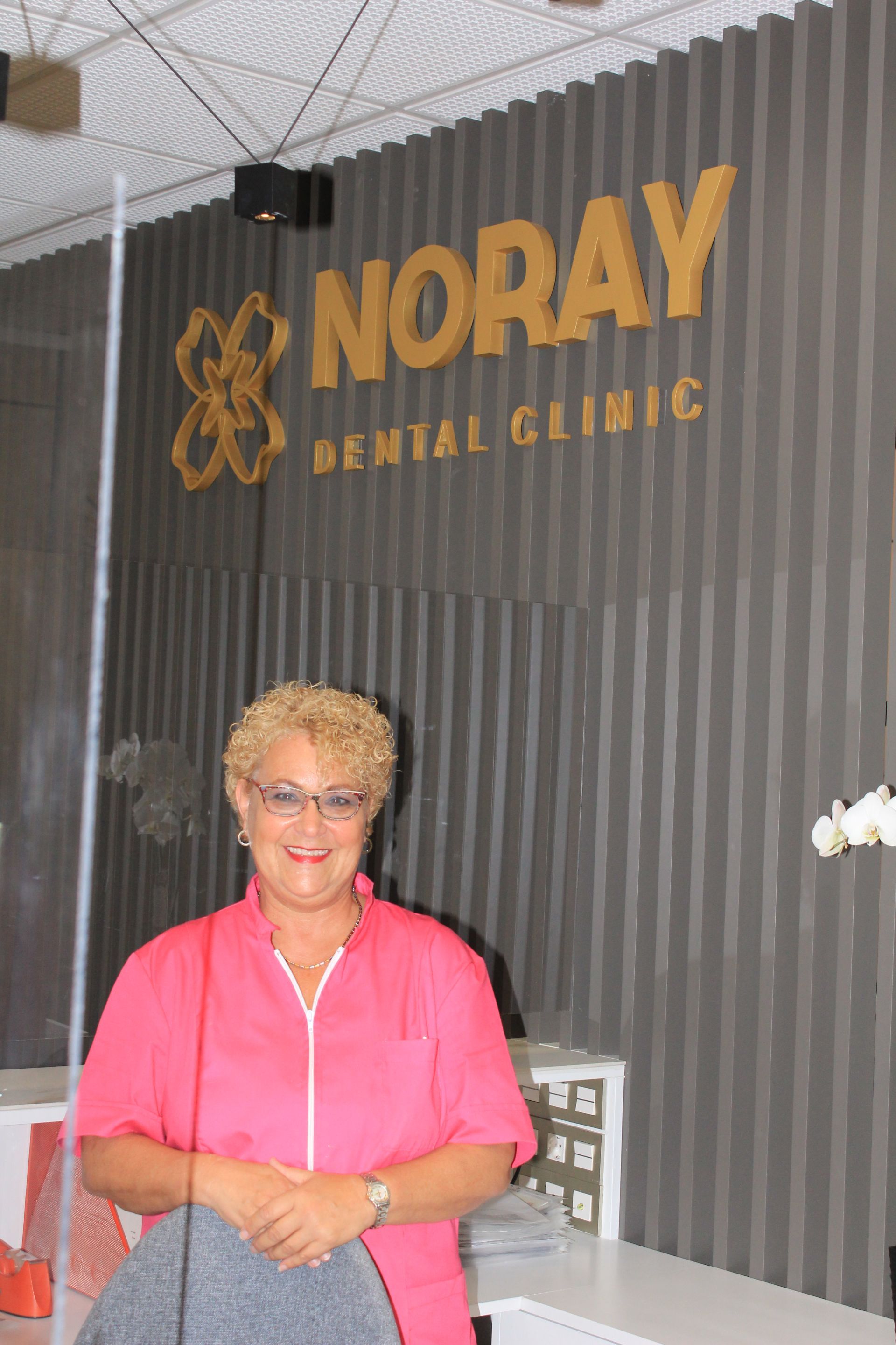 Una mujer está parada frente a un cartel de una clínica dental Noray.