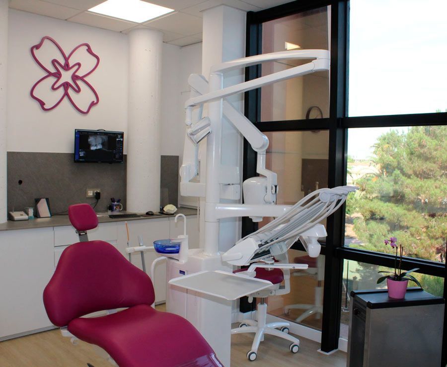 Un consultorio dental con una silla rosa y una flor en la pared.