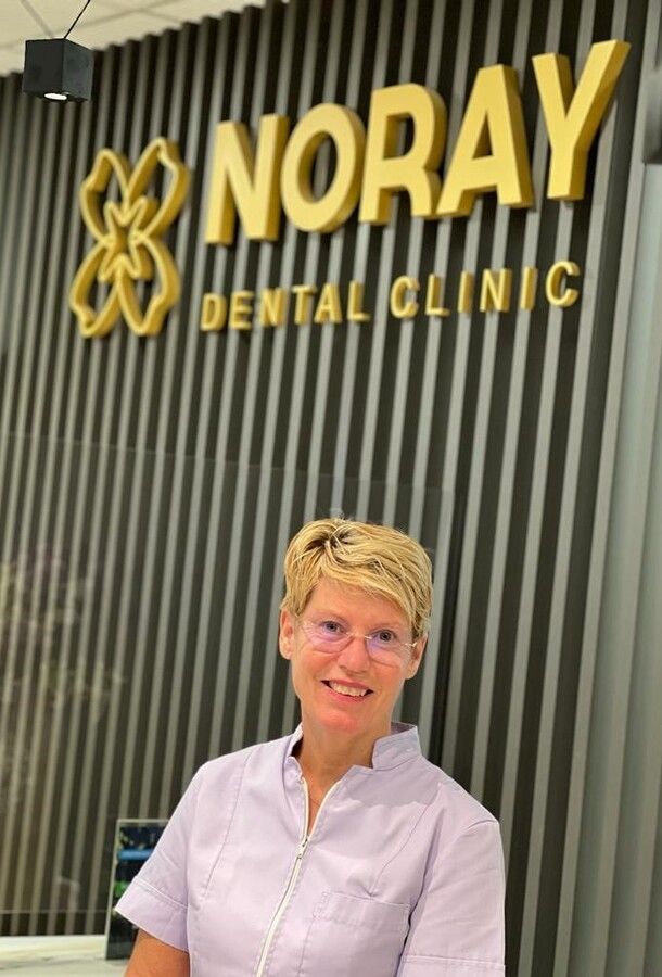 Una mujer está parada frente a un cartel de una clínica dental Noray.