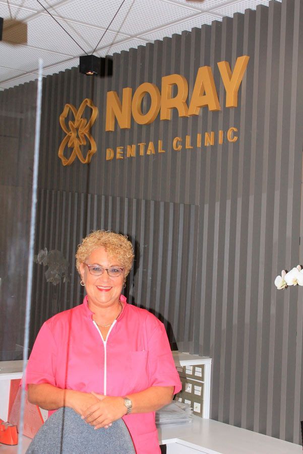 Una mujer está parada frente a un cartel de una clínica dental Noray.