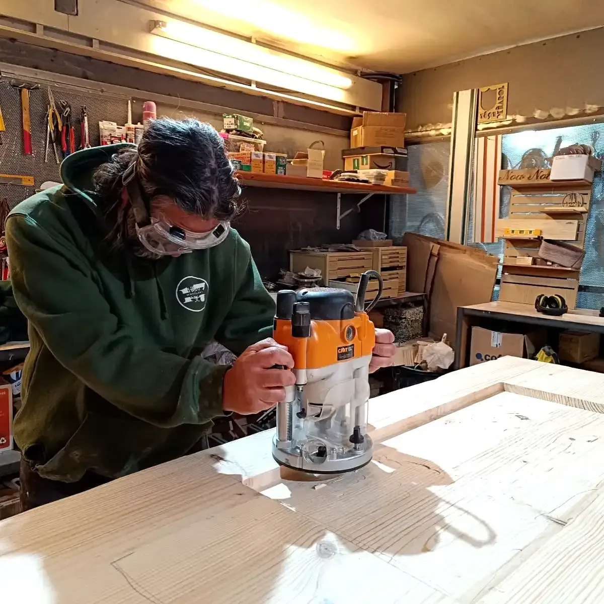 Persona utilizando una fresadora manual sobre una gran tabla de madera en un taller.