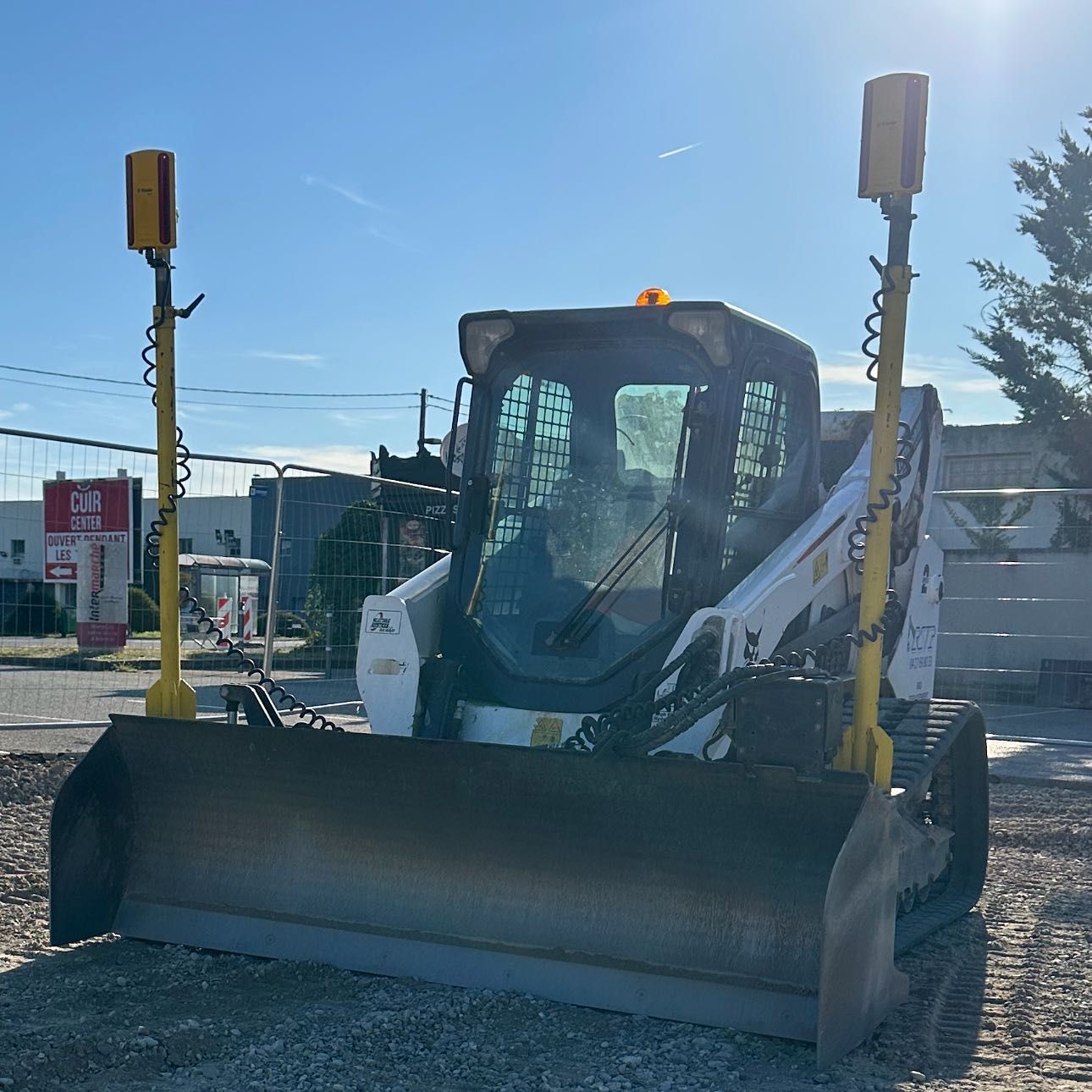 Chargeuse compacte avec godet frontal sur un terrain gravillonné sous un ciel bleu ensoleillé