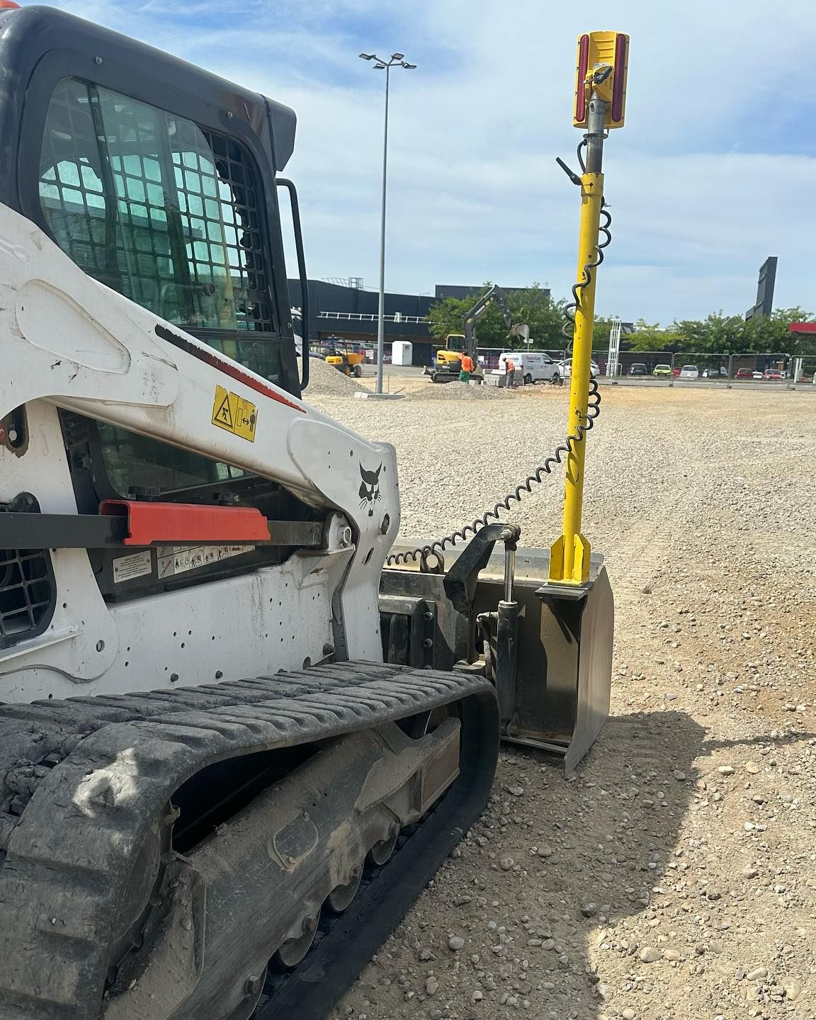 Chargeuse compacte blanche sur un chantier de gravier, vue de côté