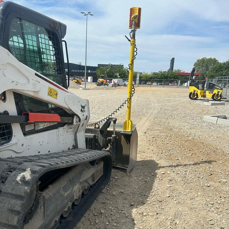 Un engin de chantier jaune sur un terrain gravillonné, à côté d'une chargeuse blanche, sous un ciel bleu.