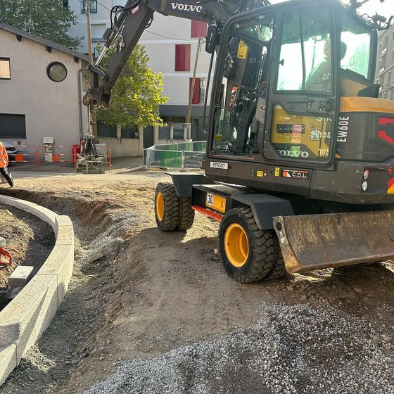 Une excavatrice sur une route de gravier sur un chantier de construction près de bâtiments et d'un rond-point.