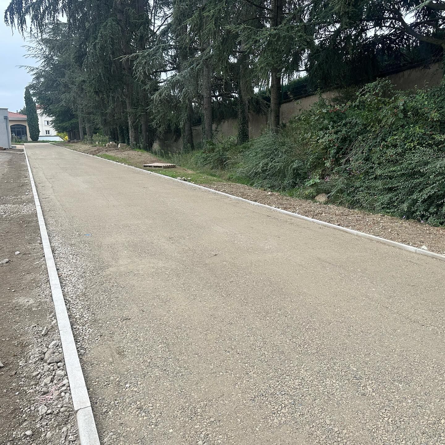 Travaux routiers sur une rue bordée d'arbres, avec un petit camion-nacelle utilitaire et une voie recouverte de gravier.