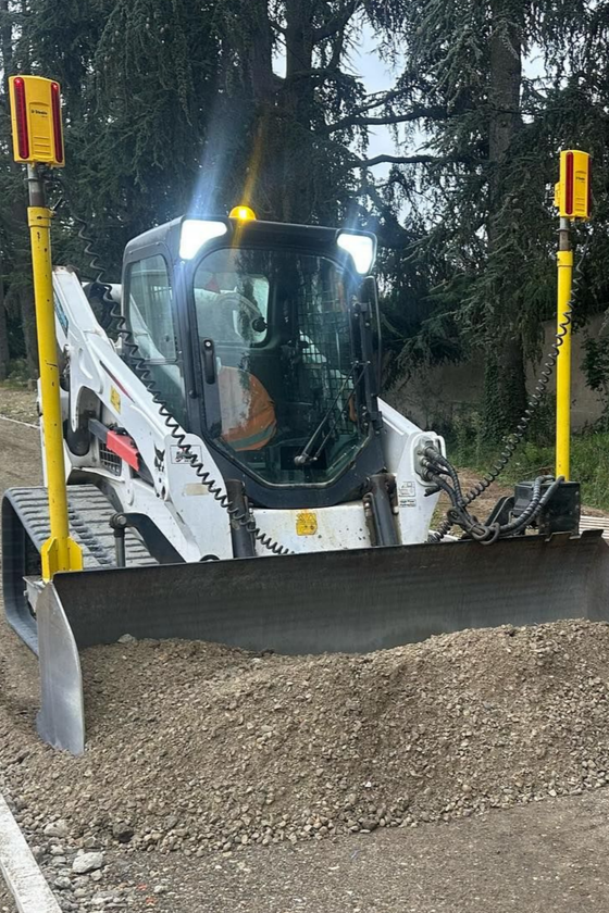 Un bulldozer à direction différentielle blanc pousse du gravier avec un godet frontal sur un chantier pluvieux
