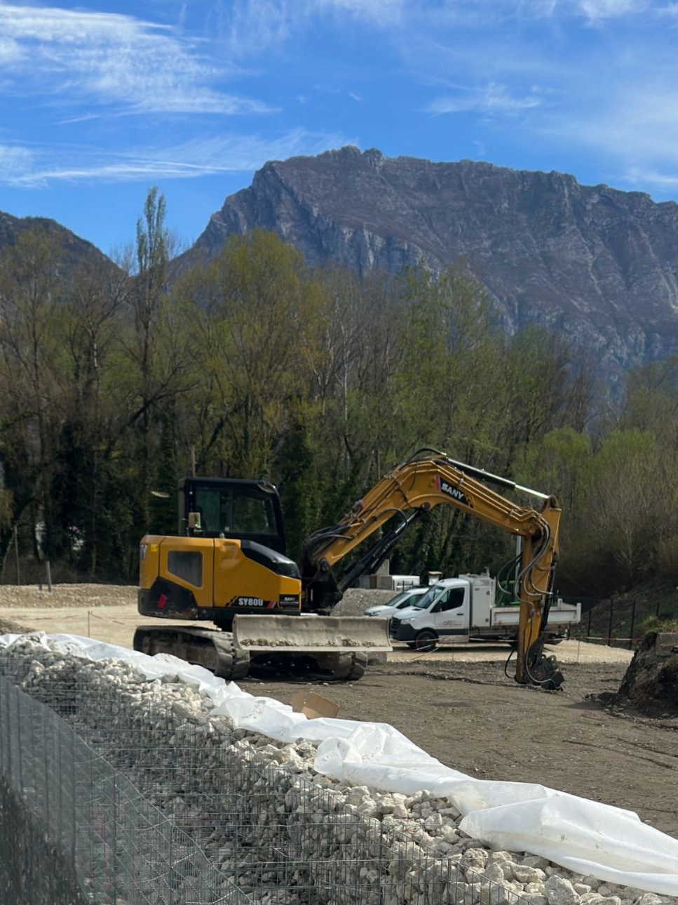 Une pelleteuse jaune à côté d'un camion blanc sur un chantier de construction avec des montagnes en arrière-plan