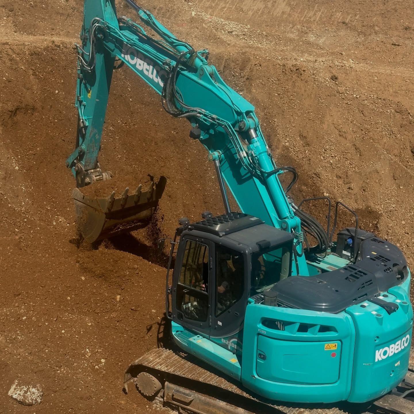 Une excavatrice turquoise creuse une fosse, godet levé.