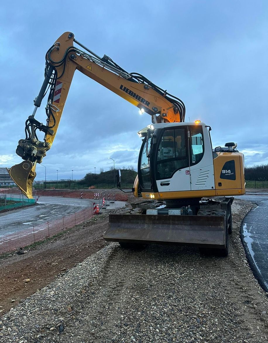 Une pelleteuse jaune sur un chantier de construction en gravier sous un ciel nuageux.
