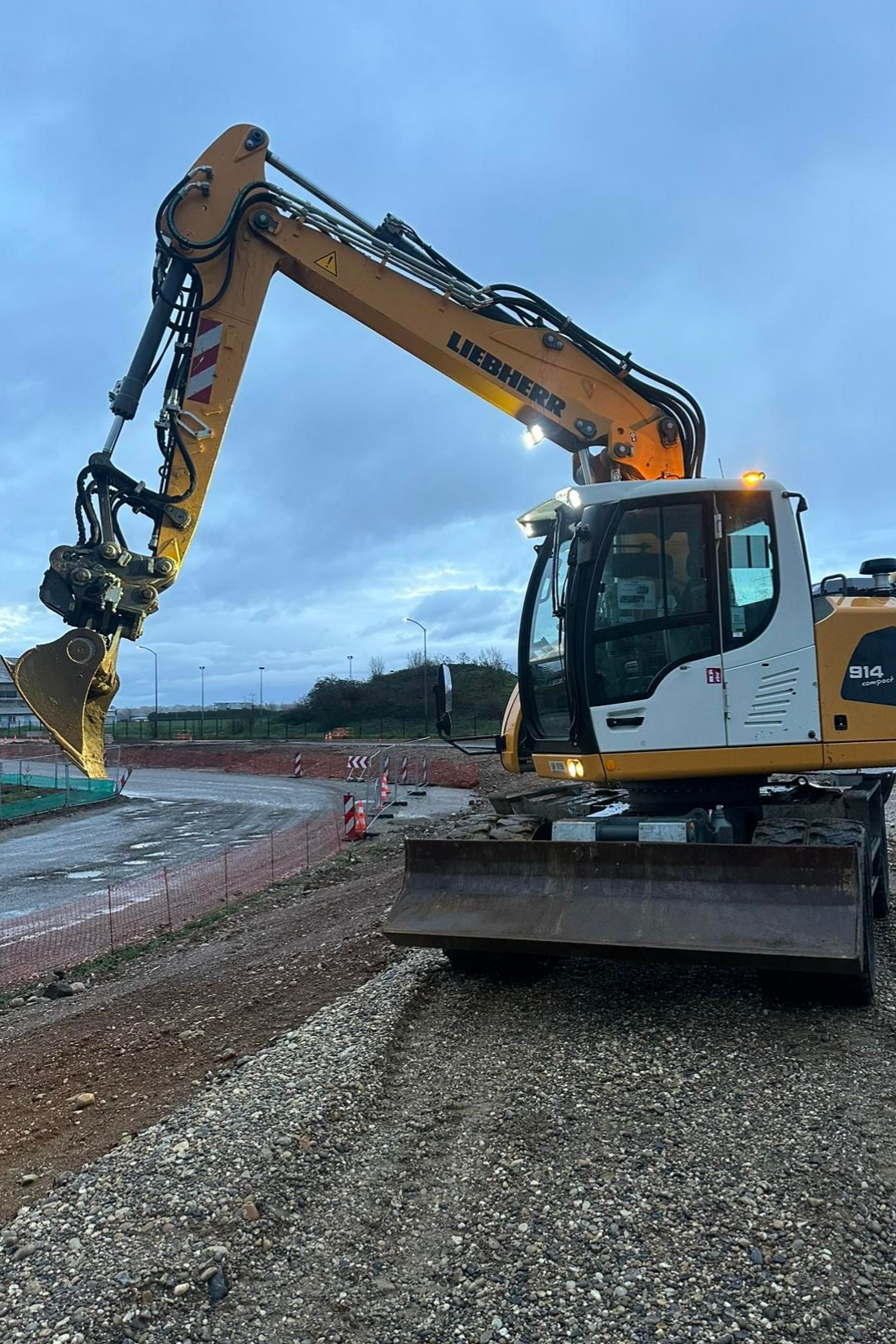 Une pelleteuse jaune sur un chantier de construction de gravier sous un ciel nuageux.