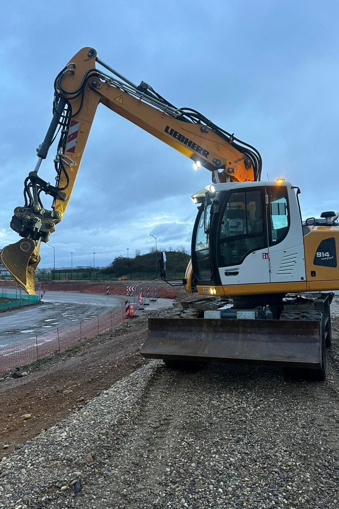 Une pelleteuse jaune sur un chantier de construction en gravier sous un ciel nuageux.