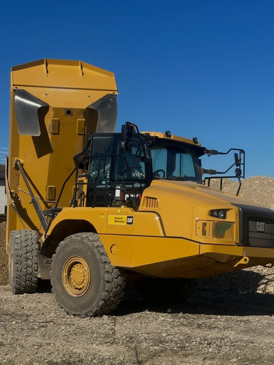 Camion-benne jaune de chantier stationné sur du gravier sous un ciel bleu dégagé