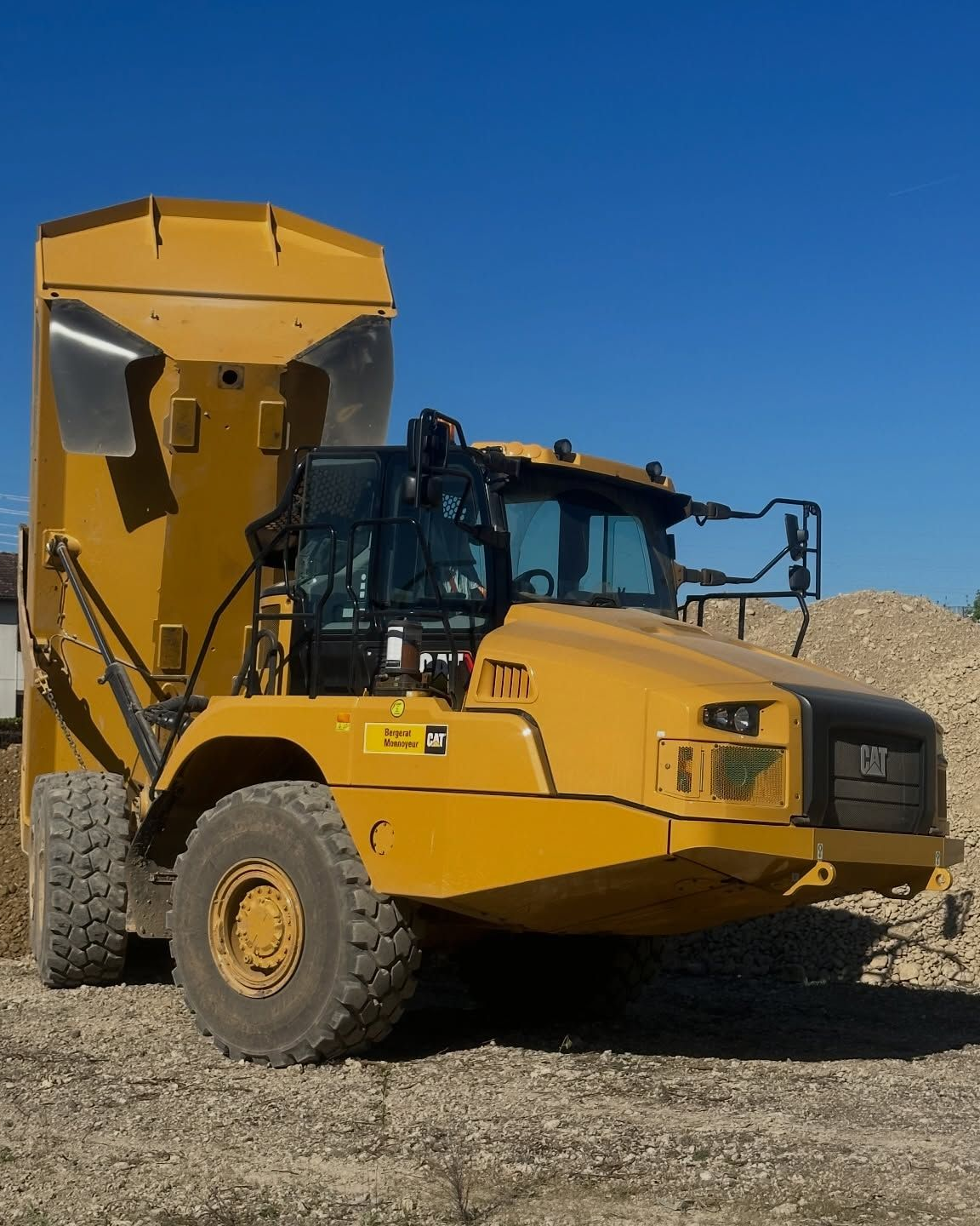 Camion-benne jaune robuste sur un site de gravier sous un ciel bleu clair