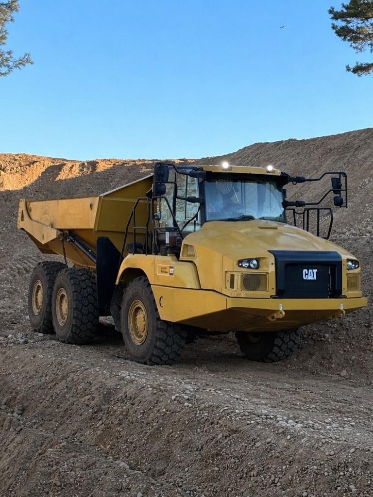 Camion-benne articulé jaune sur un chemin de gravier au milieu d'un chantier rocailleux, sous un ciel bleu.